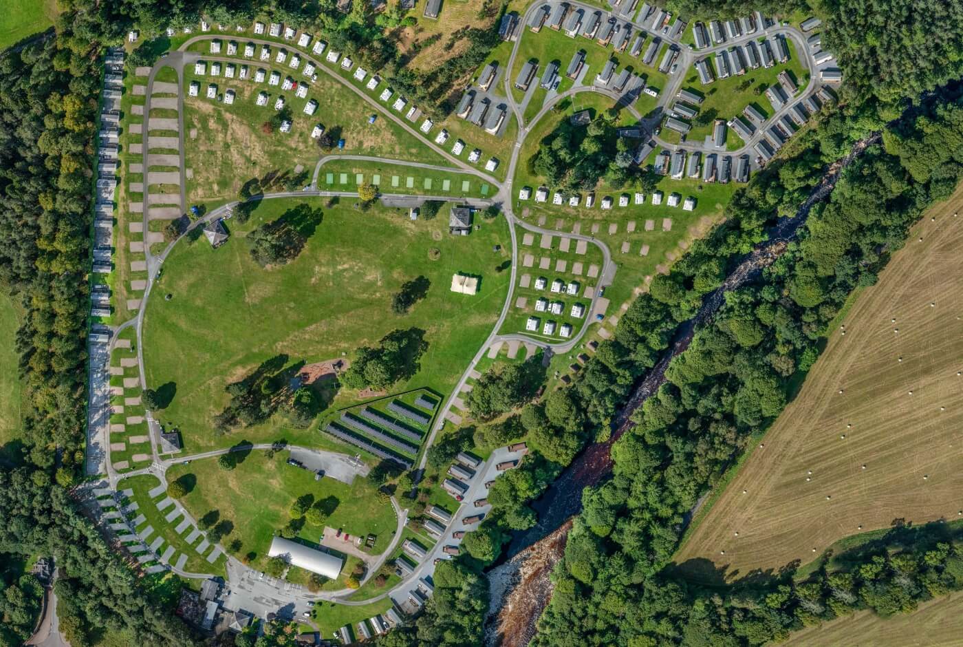 Vista aérea del Blair Castle Caravan Park con filas de caravanas residenciales en campos verdes junto a un río