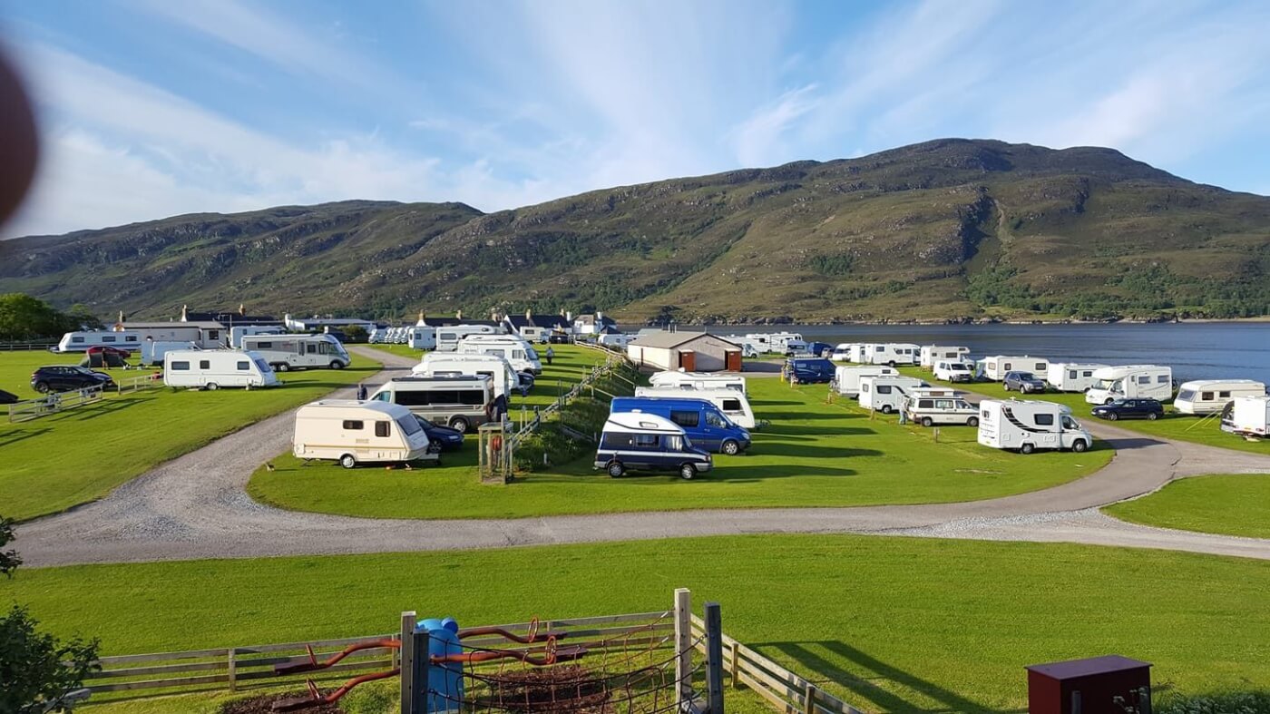 Autocaravanas y caravanas en el Broomfield Holiday Park de Ullapool junto a un loch con montañas al fondo