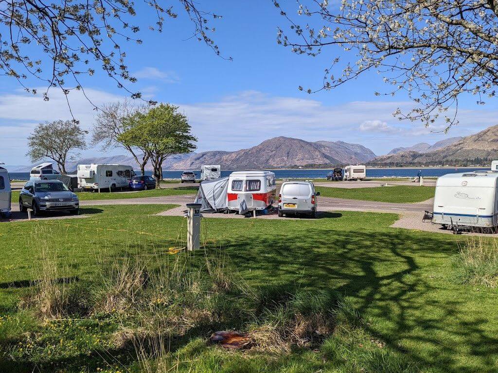 Autocaravanas y caravanas en el Bunree Caravan and Motorhome Club Site con vistas a un loch y montañas