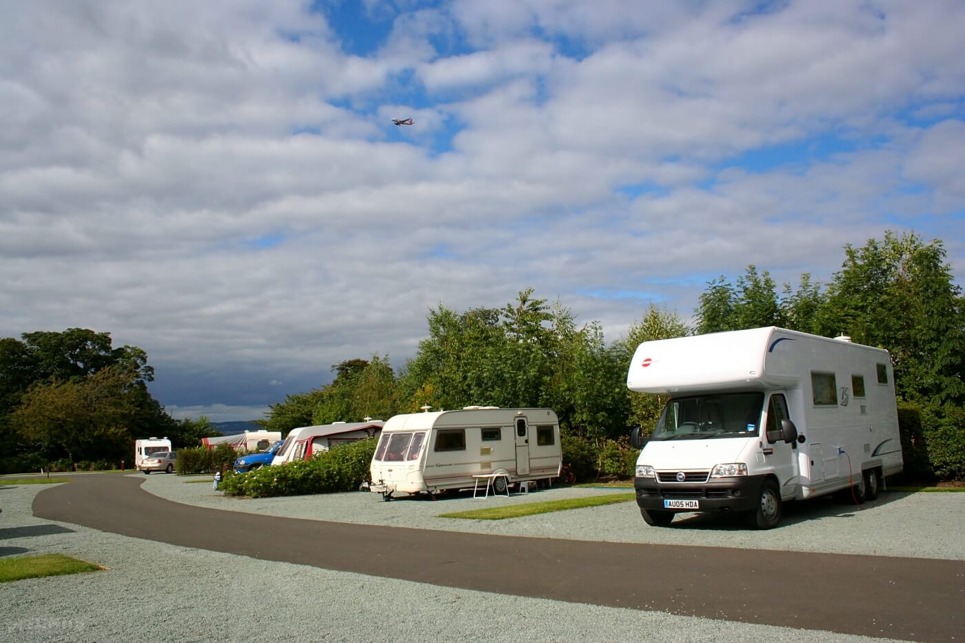 Autocaravanas y caravanas aparcadas en el Edinburgh Caravan and Motorhome Club Site con árboles y cielo nublado