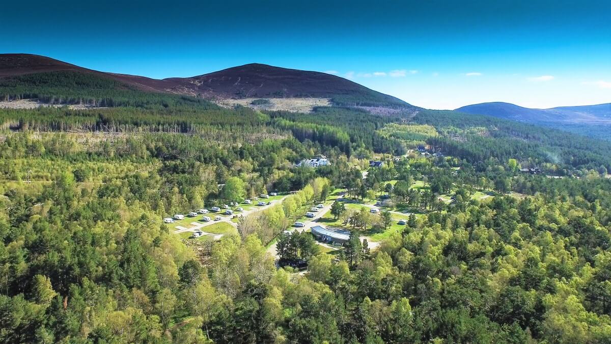 Vista aérea del Glenmore Campsite en Loch Morlich entre bosques de pinos y montañas bajo cielo azul