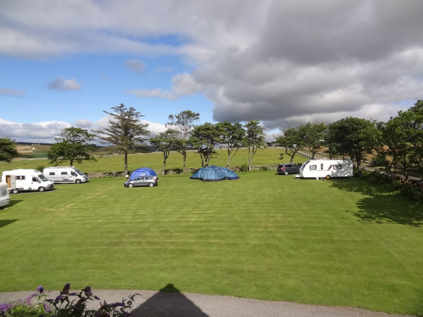 Autocaravanas, tiendas y caravanas en el Inver Caravan Park de Dunbeath en un amplio prado con árboles