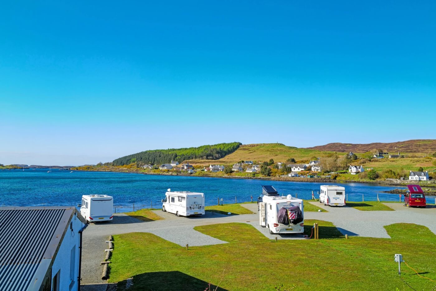 Caravanas y autocaravanas en el Kinloch Campsite junto al mar con flores silvestres en primer plano