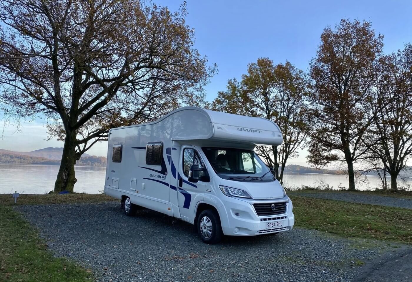 Autocaravana aparcada junto al lago en el Luss Caravan and Camp Site rodeada de árboles en otoño