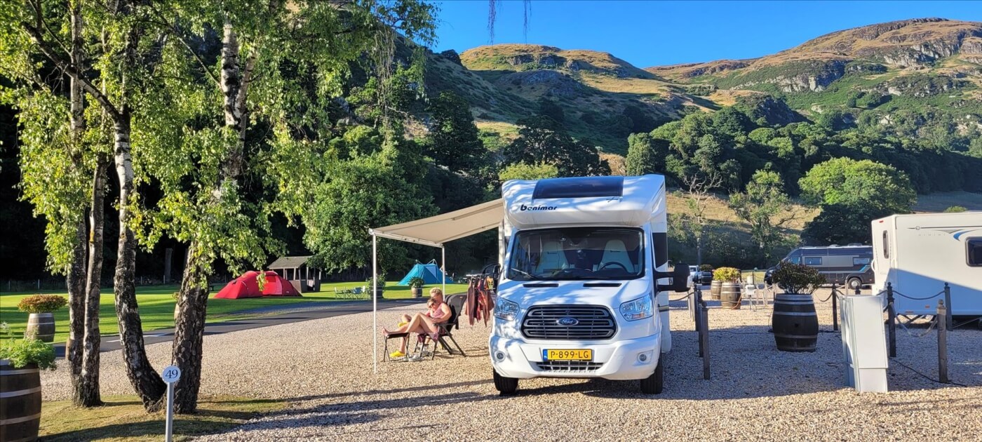 Autocaravana en el Witches Craig Caravan and Camping Park con montañas y tiendas al fondo
