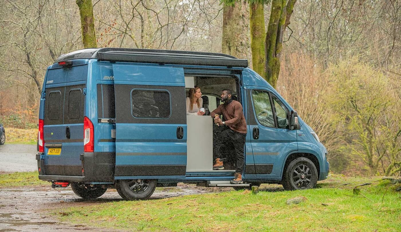 Dos personas descansan en una camper aparcada en un bosque escocés.