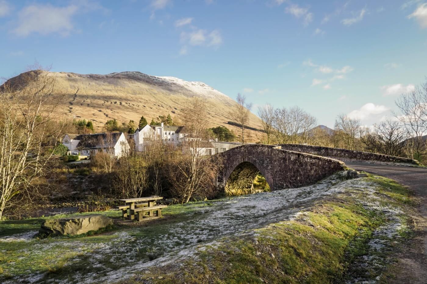 Puente de piedra y mesa de picnic ante las montañas de Bridge of Orchy.