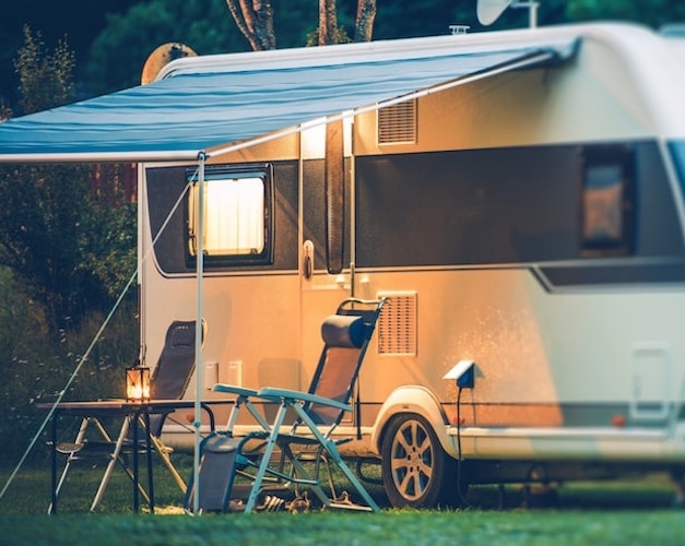 Caravana aparcada, con toldo, mesa de camping y sillas.